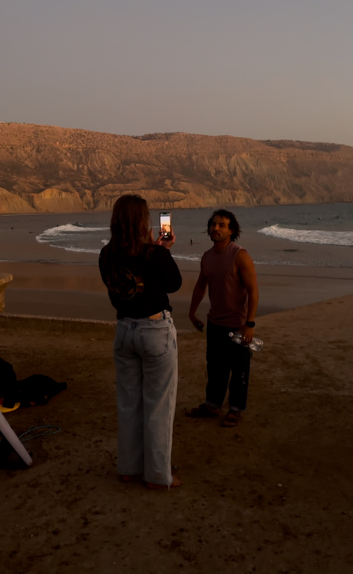 Two people at beach during sunset with cliffs in background